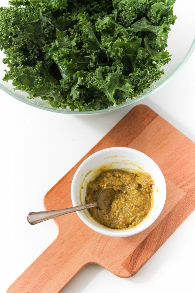 a bowl of greens with a small bowl of nutritional yeast and tahini mixture