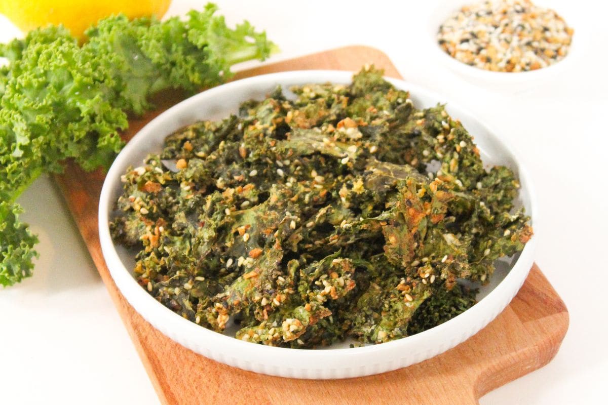 oven baked kale chips with Everything Bagel seasoning in a shallow white bowl with a lemon behind it