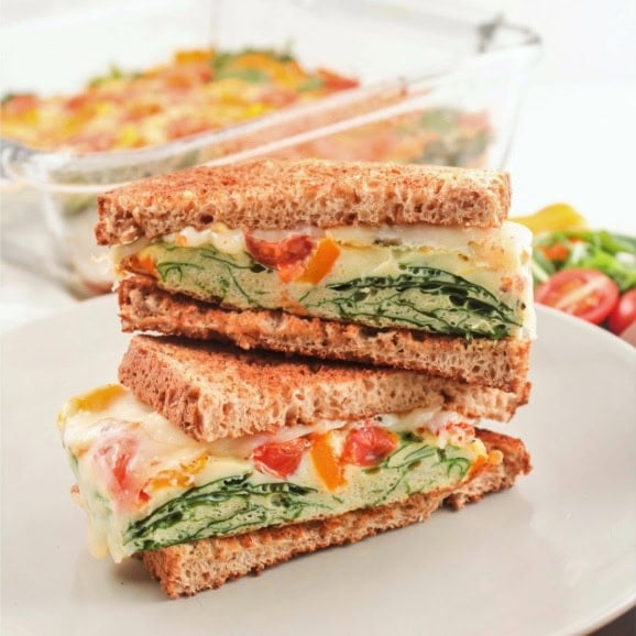 a stack of breakfast sandwiches with eggs, vegetables, and cheese on a plate