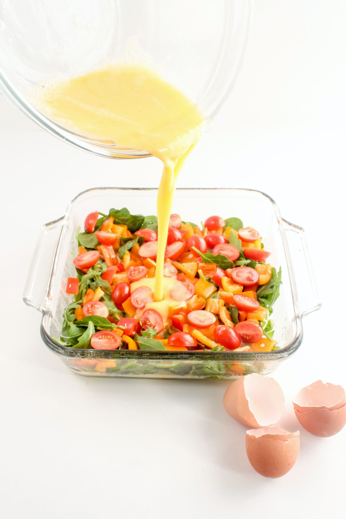 raw scrambled eggs being poured into a glass baking dish with vegetables in it