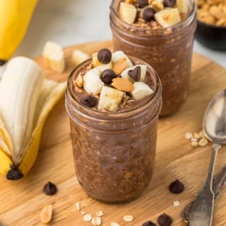 a mason jar with chocolate peanut butter overnight oatmeal topped with banana slices and chocolate chips on a wooden board