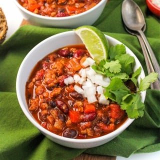 slow cooker turkey chili in a white bowl with a lime, onions, and cilantro