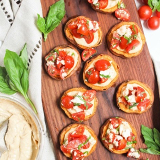 gluten free sweet potato appetizer on a wooden tray with hummus and fresh herbs