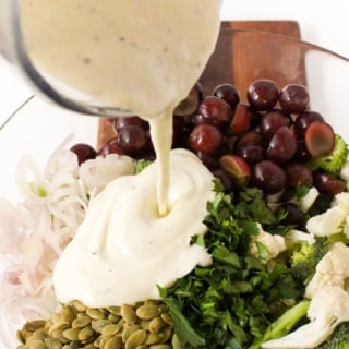 lemon Greek yogurt dressing being poured from a glass measuring cup over a salad