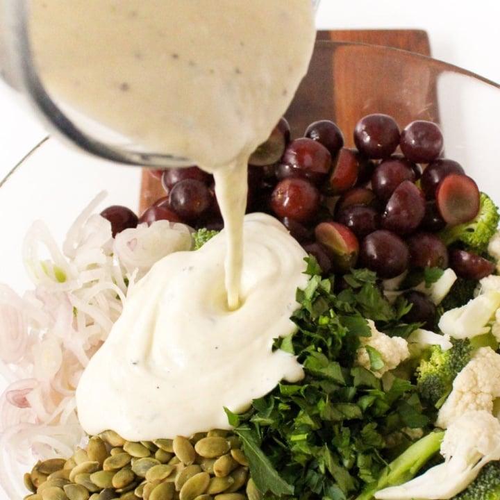 lemon Greek yogurt dressing being poured from a glass measuring cup over a salad