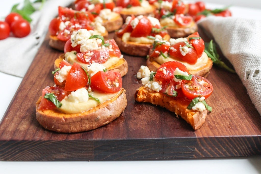 sweet potato rounds with hummus, tomatoes, and feta cheese on a wooden platter
