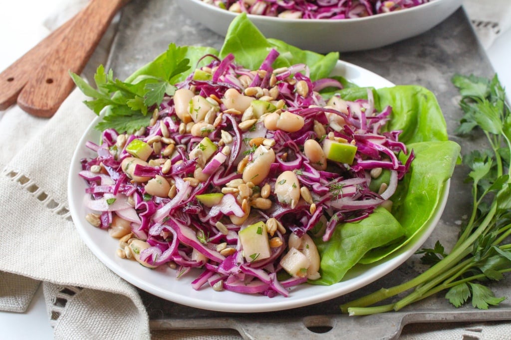 Cabbage slaw with white beans and diced apples on a white plate with butter lettuce
