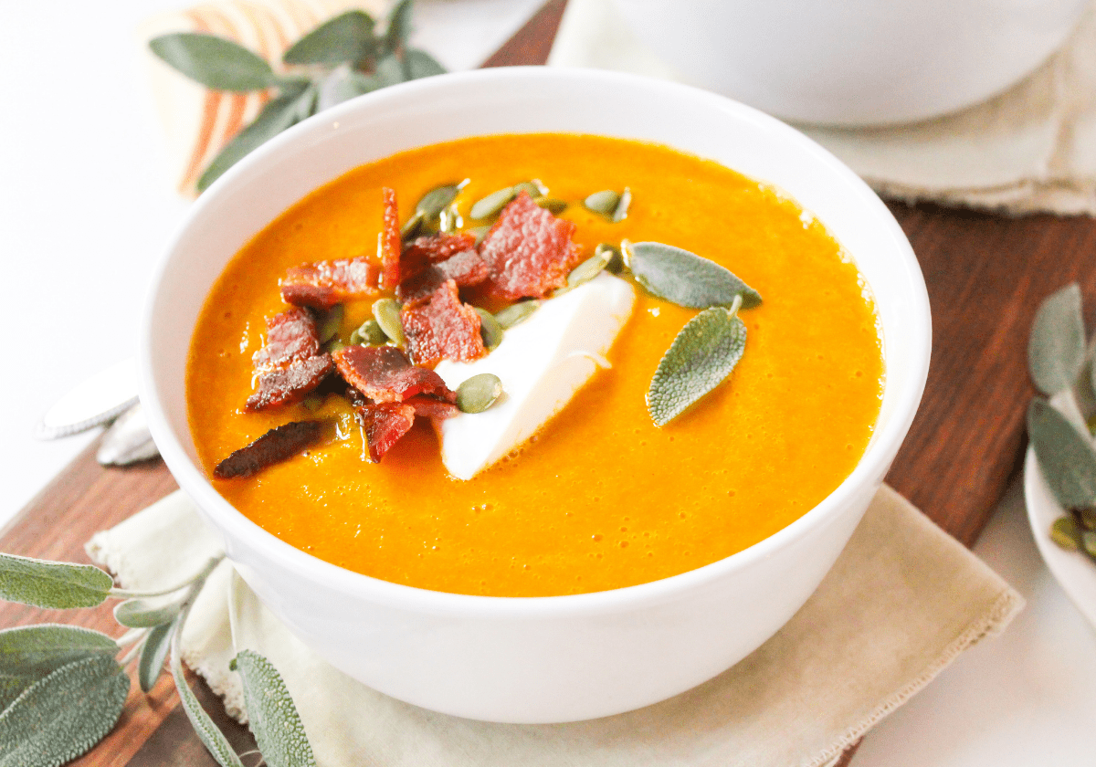 butternut squash soup with bacon, Greek yogurt, and sage leaves in a white bowl