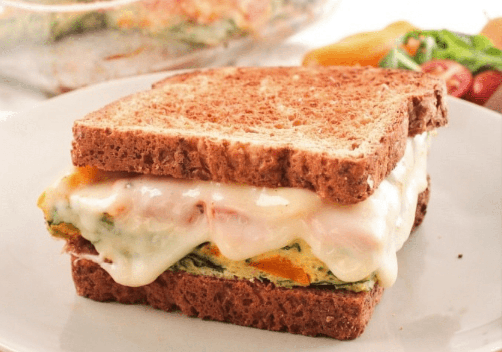 a breakfast sandwich with eggs, vegetables, and melted cheese