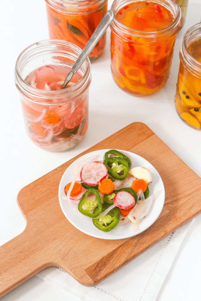 fermentd radishes and jalapenos on a wooden platter with jars of fermented vegetables in the background
