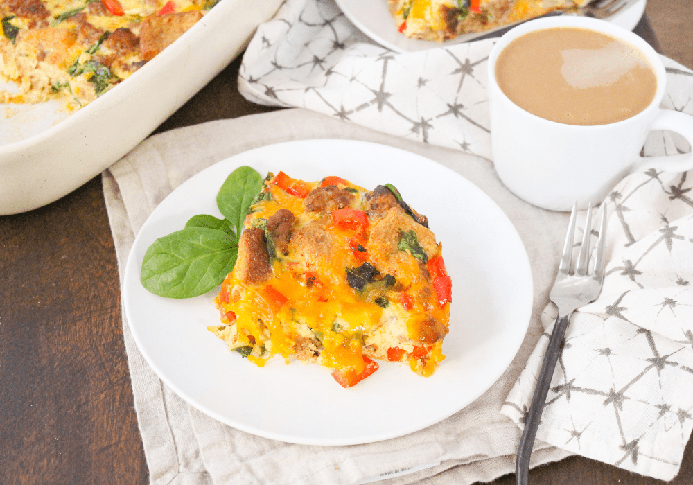 a slice of sausage egg casserole on a white plate with a mug of coffee behind it