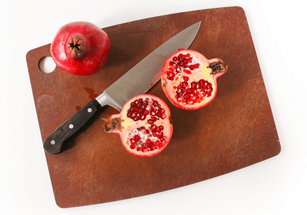 sliced pomegranate on a wooden cutting board with a knife