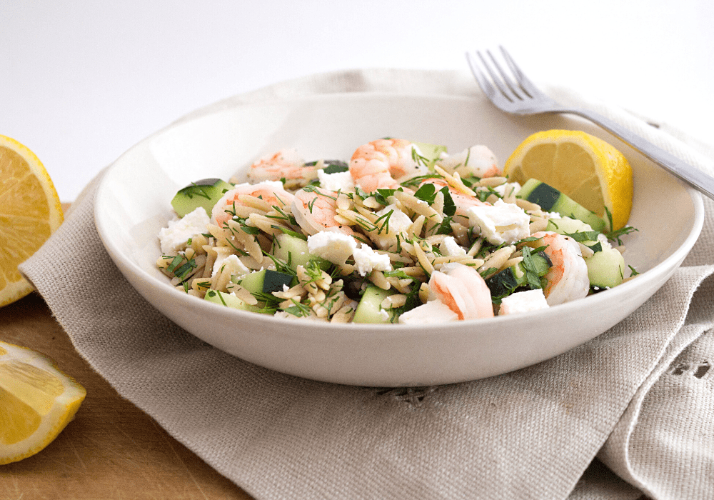 greek pasta salad with shrimp and feta in a white bowl with lemon slices
